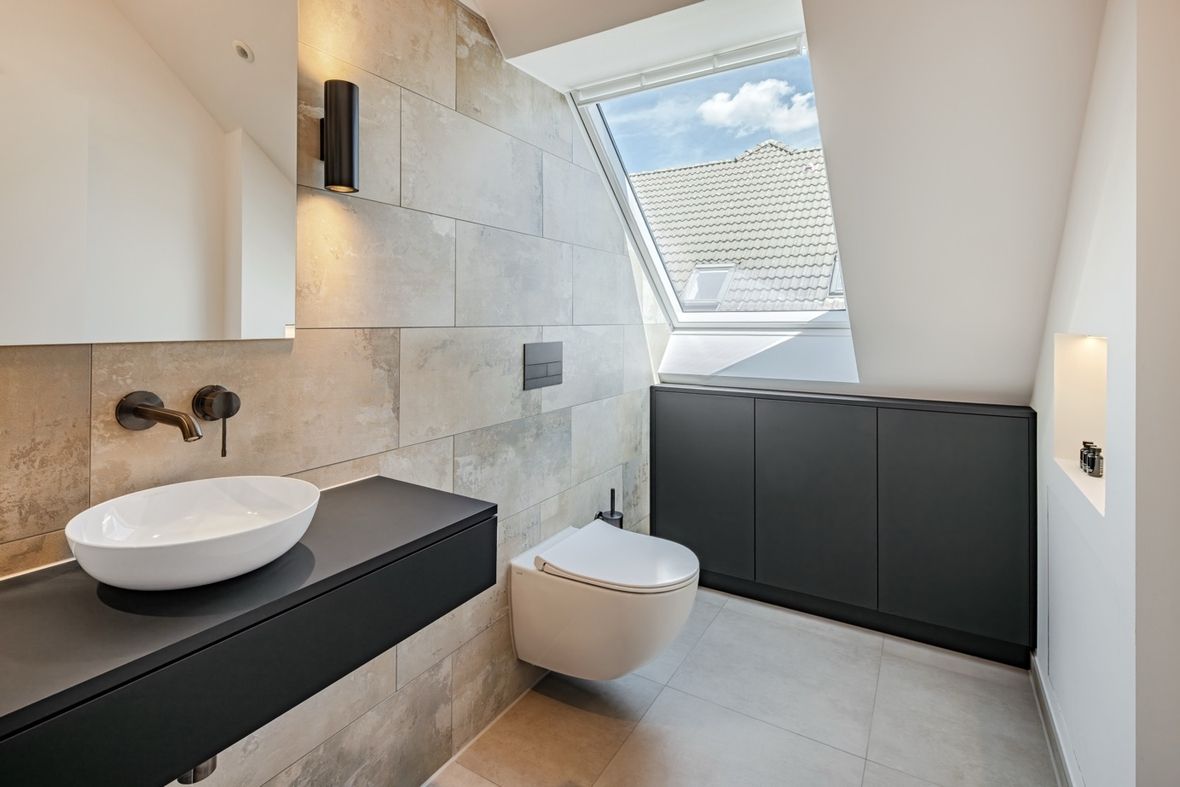 Modernes Badezimmer mit wandhängendem WC, rundem Aufsatzwaschbecken auf schwarzer Ablage und großem Dachfenster
